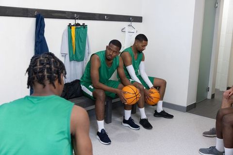 Basketball teammates sitting on bench holding basketballs showing focus and team unity