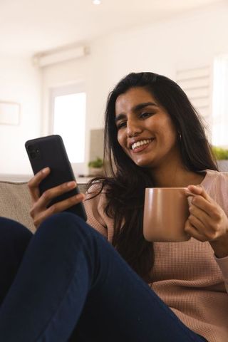 Smiling Woman Relaxing with Smartphone and Coffee at Home