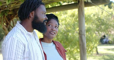 African american couple embracing under pergola in sunlit park, romantic outdoor moment