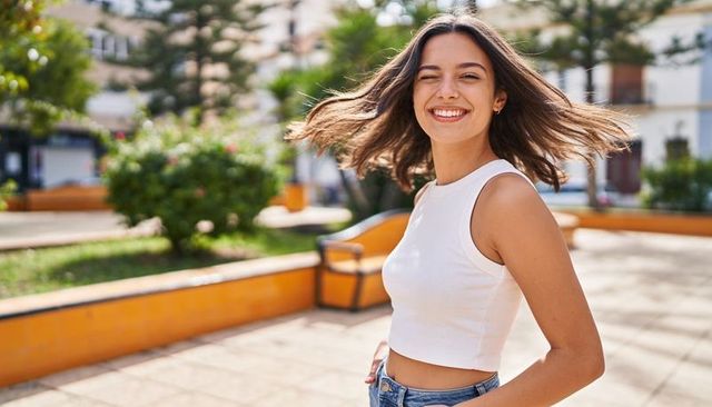 Smiling woman twirling in sunny plaza wearing white crop top and denim jeans