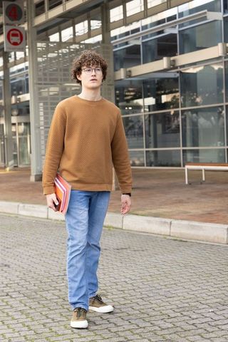 Curly-haired student walking with colorful folders on modern urban campus glass facade