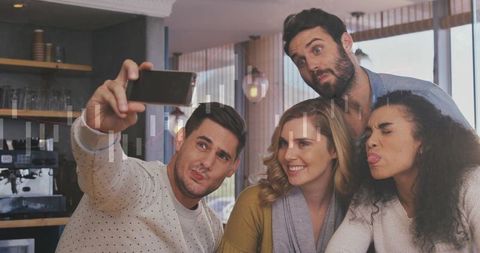 Friends taking selfie at cafe counter making faces and smiling around espresso machine