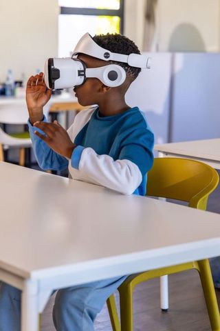 African american boy exploring virtual reality headset while learning in modern classroom