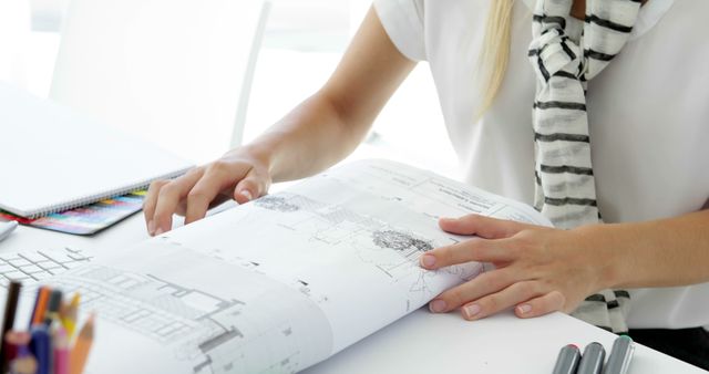 Individual reviewing architectural blueprints at a desk, ideal for illustrating design processes, project planning in architectural firms, or professional environments.