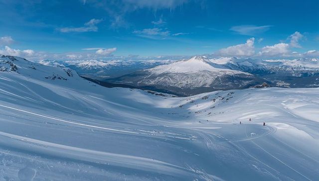 Skiers traversing pristine alpine slopes across expansive snowy valley with volcanic peak