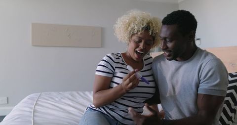 Black couple celebrating positive pregnancy test in cozy bedroom, joyful anticipation