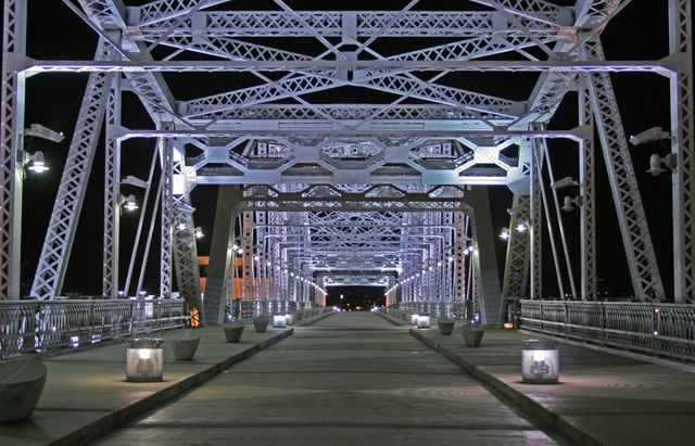 This stock image captures an illuminated steel bridge at night showcasing intricate geometric patterns created by metal trusses. Ideal for illustrating urban architecture, city nightscapes, and modern infrastructure projects. Perfect for websites, brochures, and articles focusing on city planning, engineering feats, and night photography techniques.