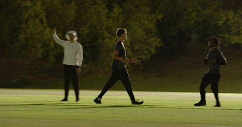 Floodlit cricket team greeting at night, black man walking onto field, high-fiving teen