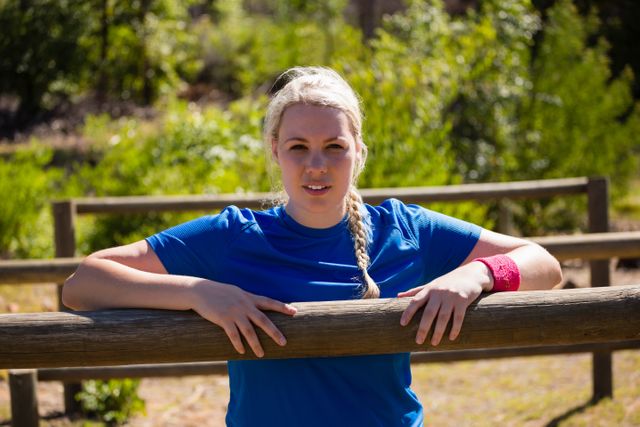 Fit woman in blue sportswear leaning on hurdles during obstacle course training in a boot camp. Ideal for promoting fitness, outdoor activities, and healthy lifestyles. Suitable for use in fitness blogs, workout guides, and health-related advertisements.