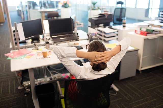 Businesswoman taking a break and relaxing on her chair at her desk in a modern office. This image can be used for articles or advertisements related to workplace wellness, stress management, productivity tips, corporate culture, and work-life balance. It is also suitable for illustrating business environments and professional settings.
