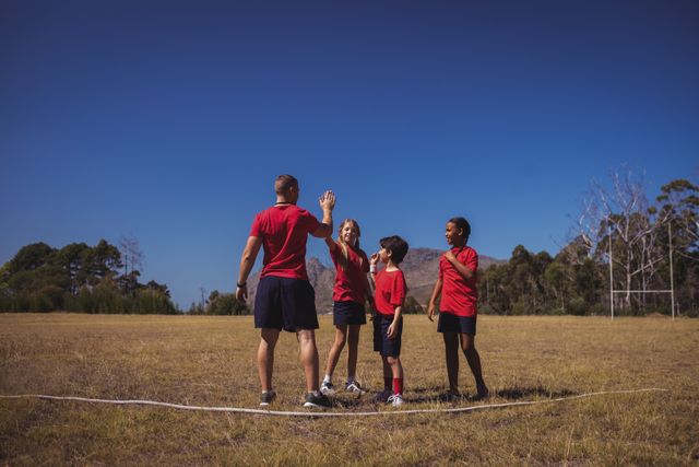 Trainer and children high-fiving during outdoor boot camp training. Ideal for use in articles or advertisements about fitness, teamwork, children's activities, summer camps, and outdoor sports.