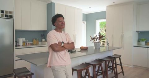 African man leaning on modern kitchen island wearing pink t-shirt and smartwatch