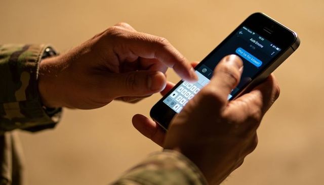 Soldier typing on smartphone in warm low light wearing camouflage uniform sleeves