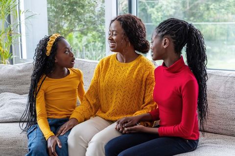 African American mother and daughters sharing conversation and holding hands on sofa