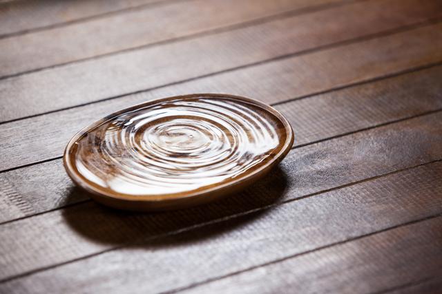 Water ripples in a wooden bowl on a rustic wooden table. Ideal for use in wellness, spa, and meditation contexts. Perfect for promoting relaxation, tranquility, and simplicity. Can be used in advertisements, websites, and social media posts related to natural materials and minimalist lifestyles.