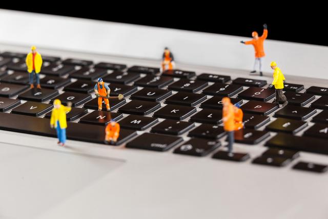 Conceptual image of miniature workmen repairing a laptop keyboard 
