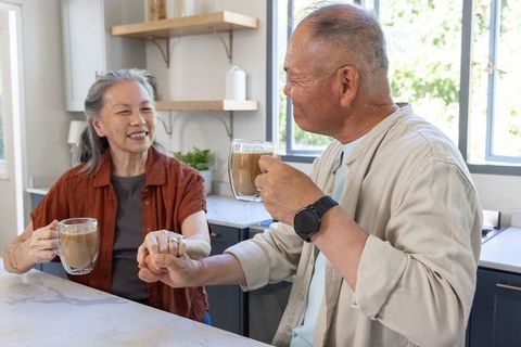 Senior asian couple sharing coffee and holding hands on kitchen counter morning affection