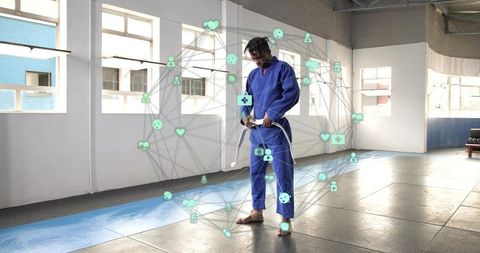Martial artist tying white belt in blue gi inside dojo with digital health network overlay