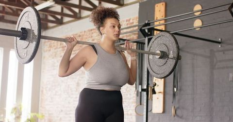 Female athlete lifting barbell in bright loft gym focusing on strength and determination