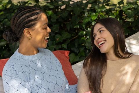 Diverse women laughing on sunlit garden bench, candid friendship moment