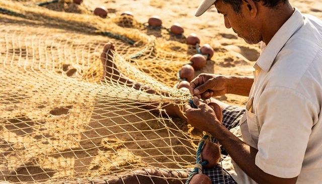 Indian fisherman mending fishing net on sunlit beach closeup hands repairing rope floats