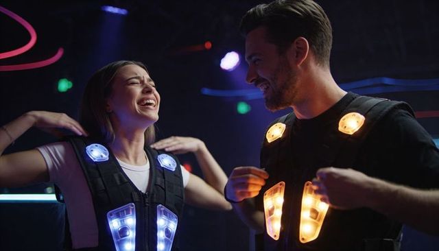 Laughing couple playing laser tag with illuminated led vests in neon arcade night