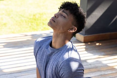 African american man relaxing with eyes closed on sunlit wooden deck with slatted shadows