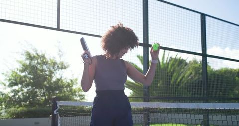 Sunlit african american woman playing tennis holding racket and ball on outdoor court