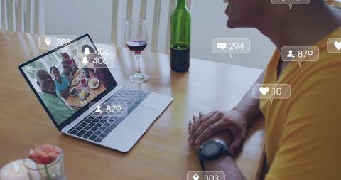 Man video-calling multigenerational family on laptop at candlelit dining table with wine