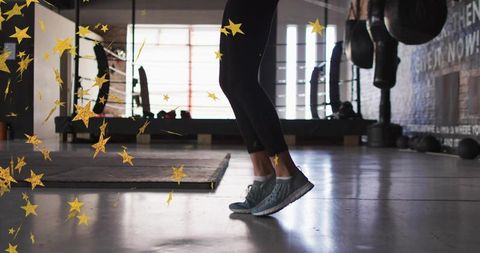 Female athlete jumping in gym showing lower legs and gray sneakers during backlit workout session
