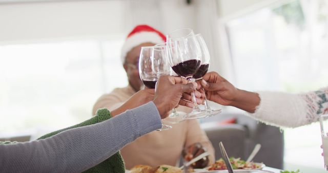 Family members toasting glasses of red wine at holiday table, wearing festive attire. Use for holiday celebration promotions, togetherness concepts, advertisements for festive occasions, and family-oriented ads.