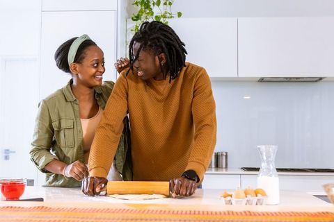 African american couple rolling dough together on bright modern kitchen island smiling