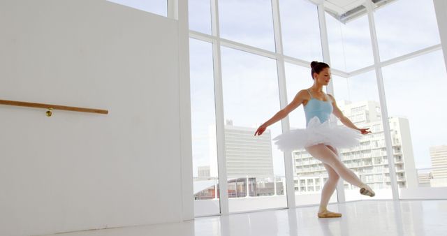 Elegant ballerina practicing ballet in bright studio with urban city view. Perfect for promoting dance classes, fitness routines, and artistic expression. Ideal for articles or media focusing on the beauty and discipline of ballet, ballet schools, and lifestyle blogs associated with dance and performing arts.