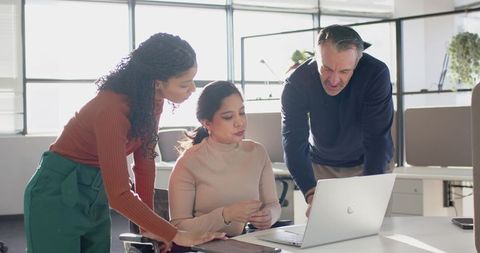 Multicultural Team Collaborating Over Laptop in Bright Open-Plan Office Discussing Strategy