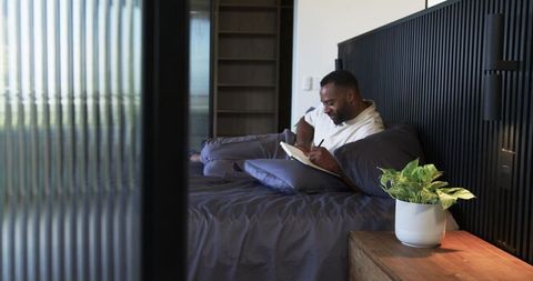Mature man journaling on bed in modern minimalist bedroom with plant, neutral tones