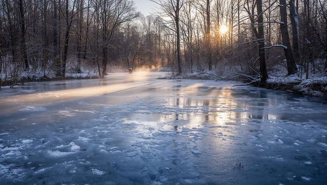 Sunlit frozen river with rising mist in winter forest dawn reflections and golden rays