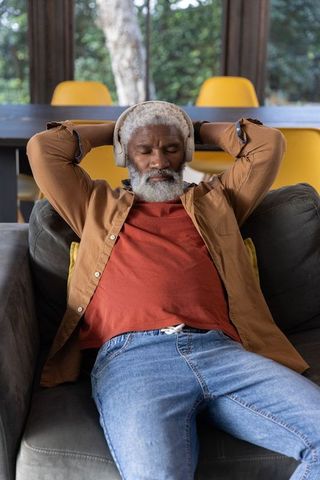 Senior african american man relaxing on sofa listening to music with wireless headphones