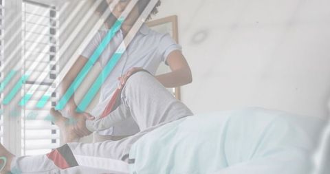 Caregiver assisting senior patient with leg stretch at bedside in sunlit room