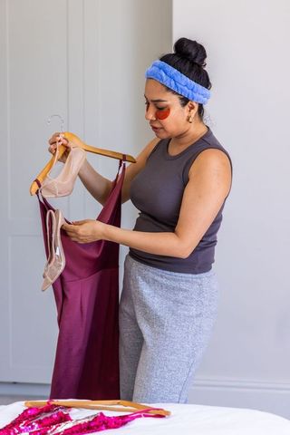 Woman holding burgundy dress and inspecting nude sandals on wooden hanger styling outfit