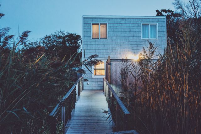Residence illuminated at dusk surrounded by nature. Ideal for articles on modern architecture, coastal living, serene retreats, vacation rentals or property listings. Could be used for promoting peaceful lifestyle or architectural designs.