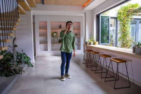 Asian man talking on smartphone in bright minimalist kitchen with indoor plants and courtyard