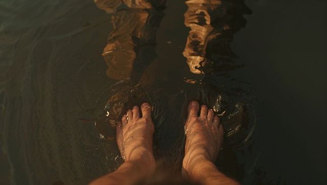 Wading bare feet creating golden ripples in shallow water at sunset