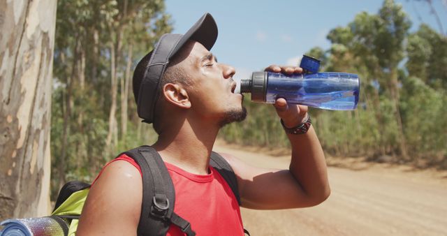 Biracial man trekking on mountain road refreshing himself, drinking water from bottle. Long distance walking, fitness and healthy outdoor lifestyle.