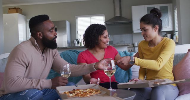 Image of happy, diverse male and female friends sharing wine and pizza at home, in slow motion. Free time, friendship and lifestyle concept.