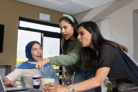 Multicultural women collaborating around laptop pointing at screen during team meeting