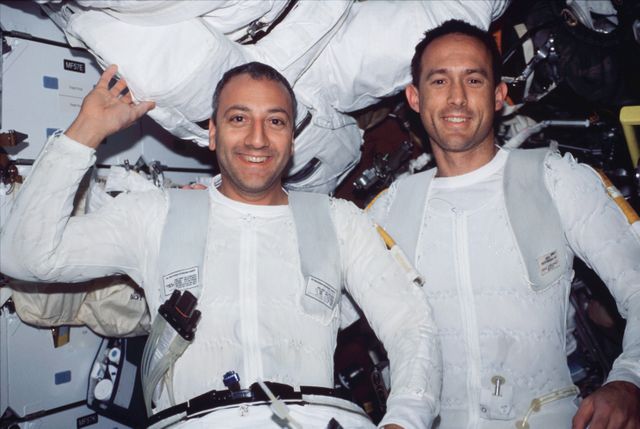 Astronauts Michael J. Massimino and James H. Newman are seen smiling after a successful spacewalk on the Space Shuttle Columbia, part of the STS-109 mission. They are in the mid deck and are starting to remove their extravehicular mobility unit space suits. The image highlights teamwork, perseverance, and achievements in space exploration. Suitable for articles related to space missions, astronaut career profiles, STEM education, and inspiring teamwork stories.