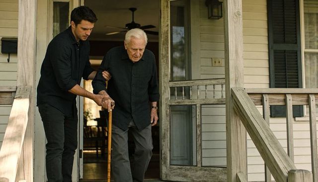 Adult caregiver assisting elderly man descending wooden porch steps with cane and support
