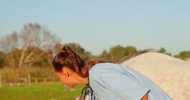 Image of a female veterinarian bending over while interacting with a horse in a rural pasture setting. The veterinarian is wearing a blue uniform and appears to be examining or communicating with the horse. Ideal for use in content related to veterinary care, animal husbandry, rural life, or veterinary medicine.