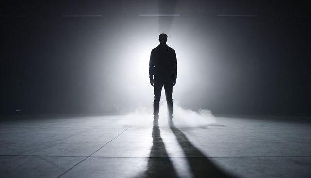 Backlit silhouette standing in foggy industrial warehouse casting long cinematic shadows