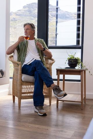Mature man relaxing with tea and notebook by sunny window overlooking mountains